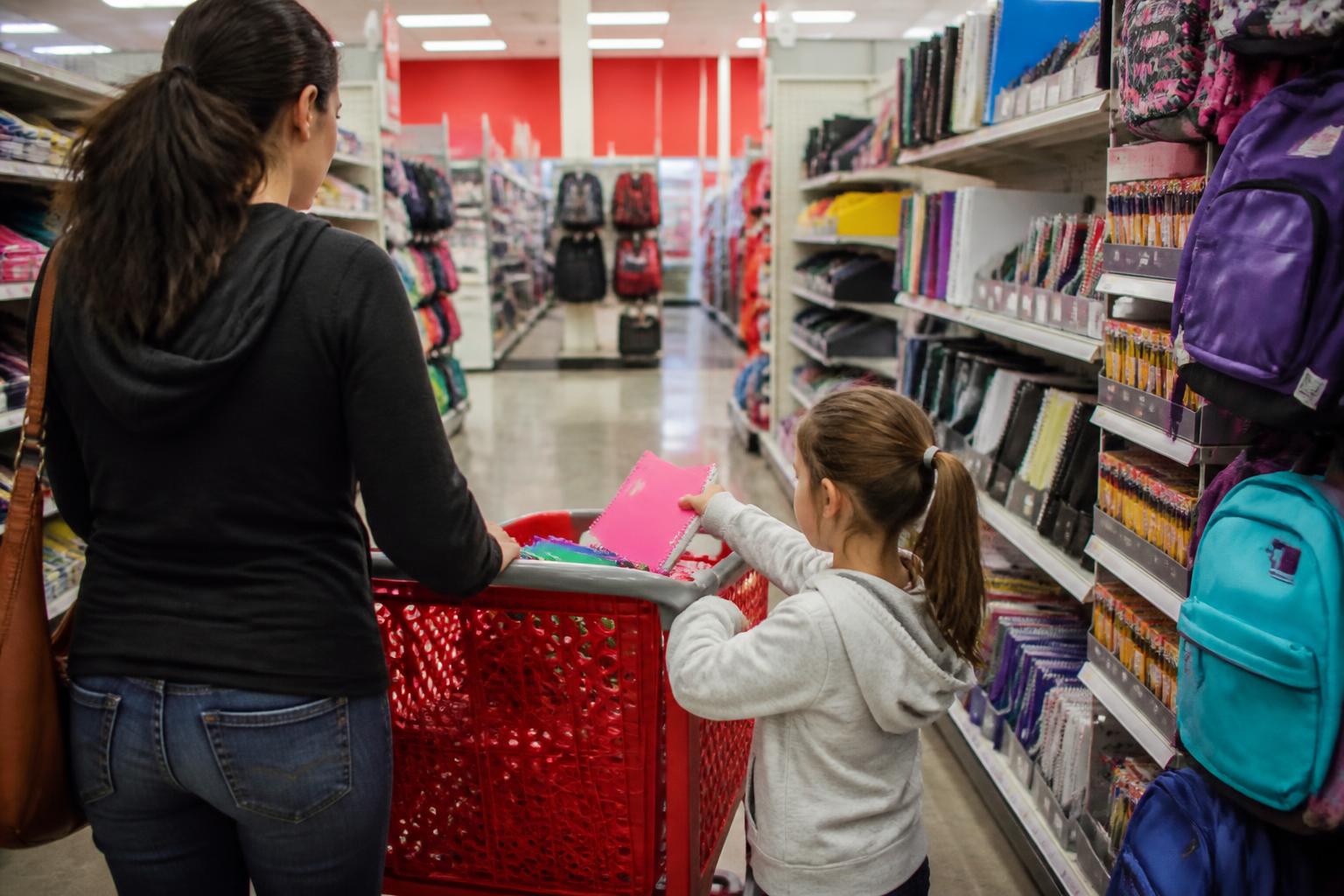 A parent and child shopping from a list in a school-supply aisle.