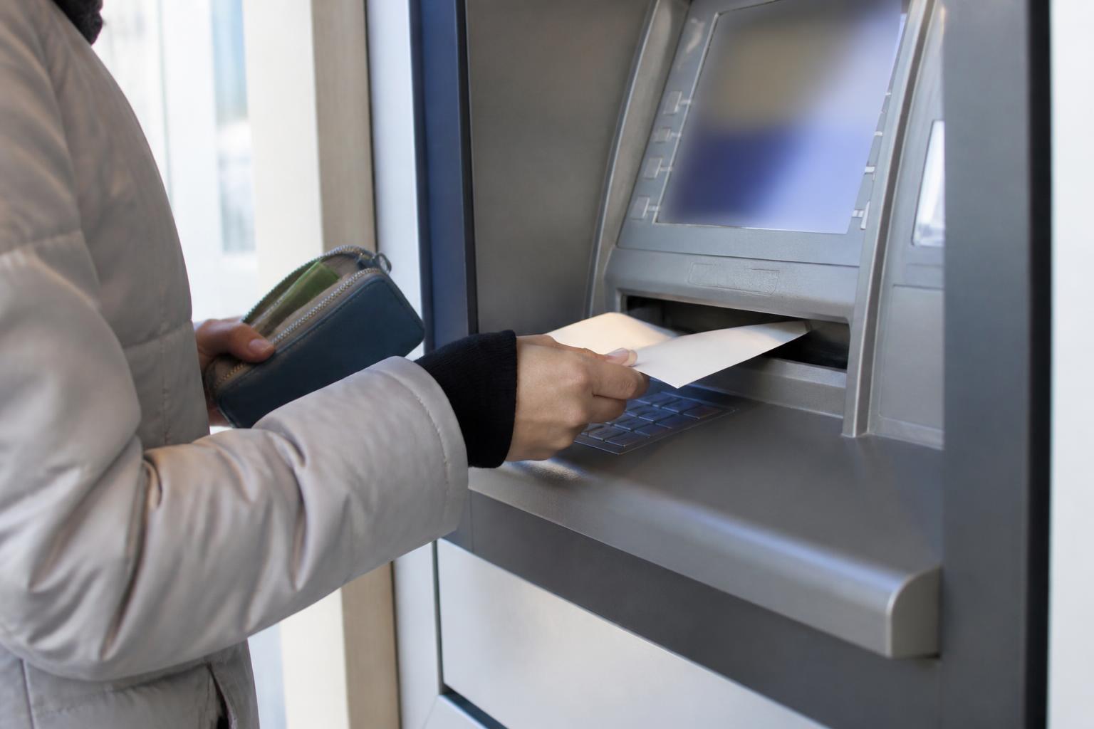 A person depositing a refund envelope at an ATM while holding a savings pouch.