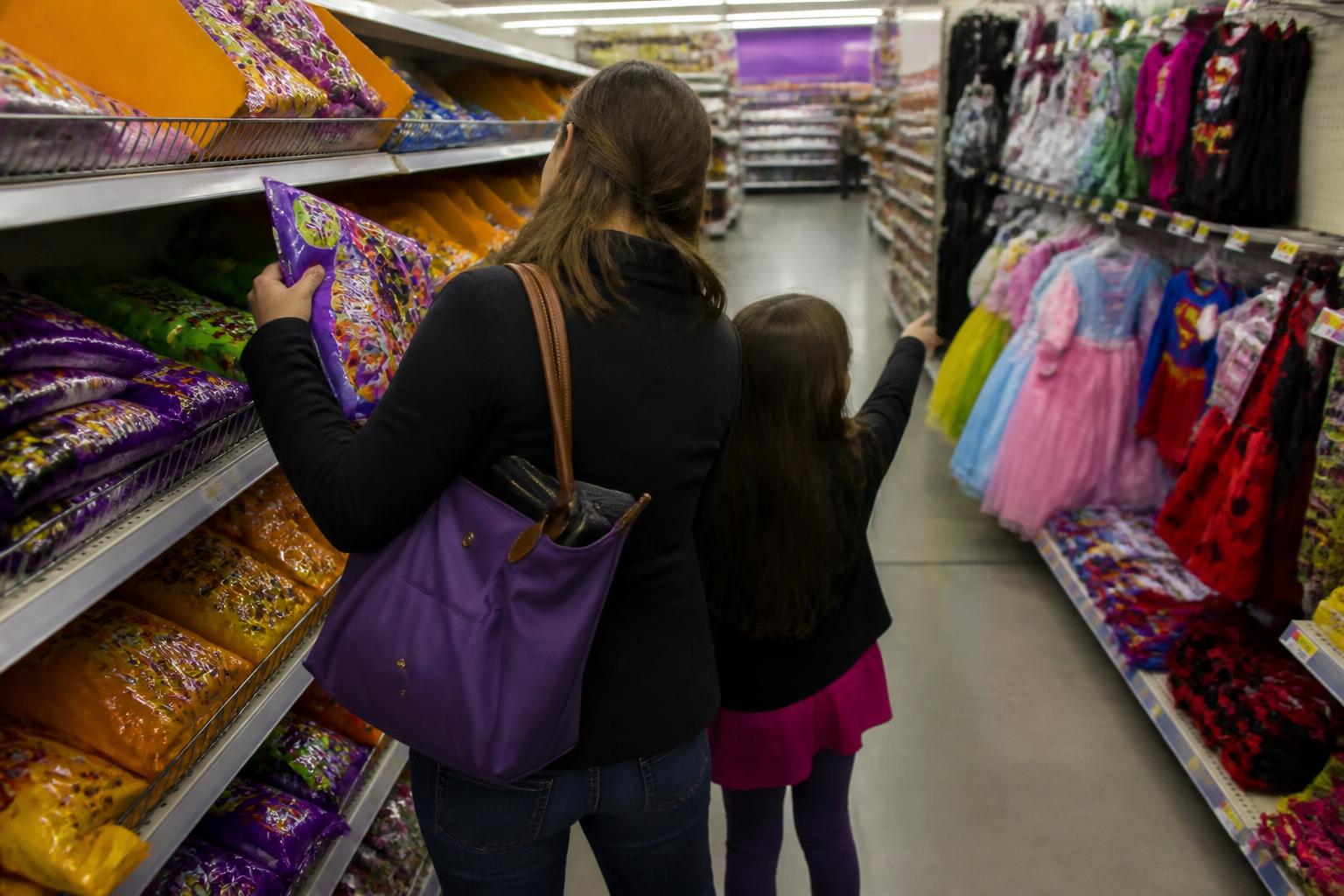 A parent and child shopping in a Halloween aisle with a zipped wallet in a tote.