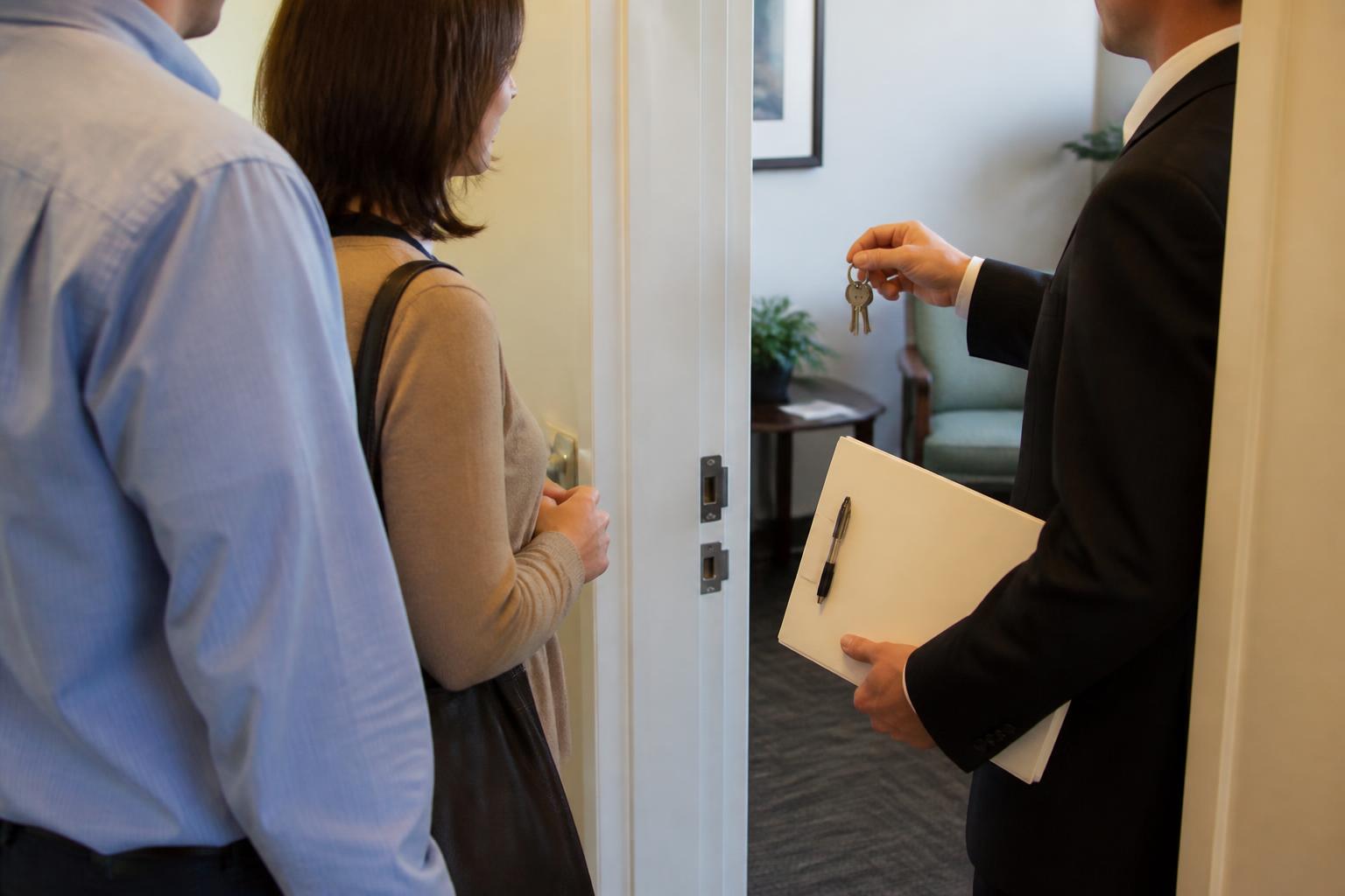 A homebuyer pausing outside a mortgage closing room with keys and a blank folder.