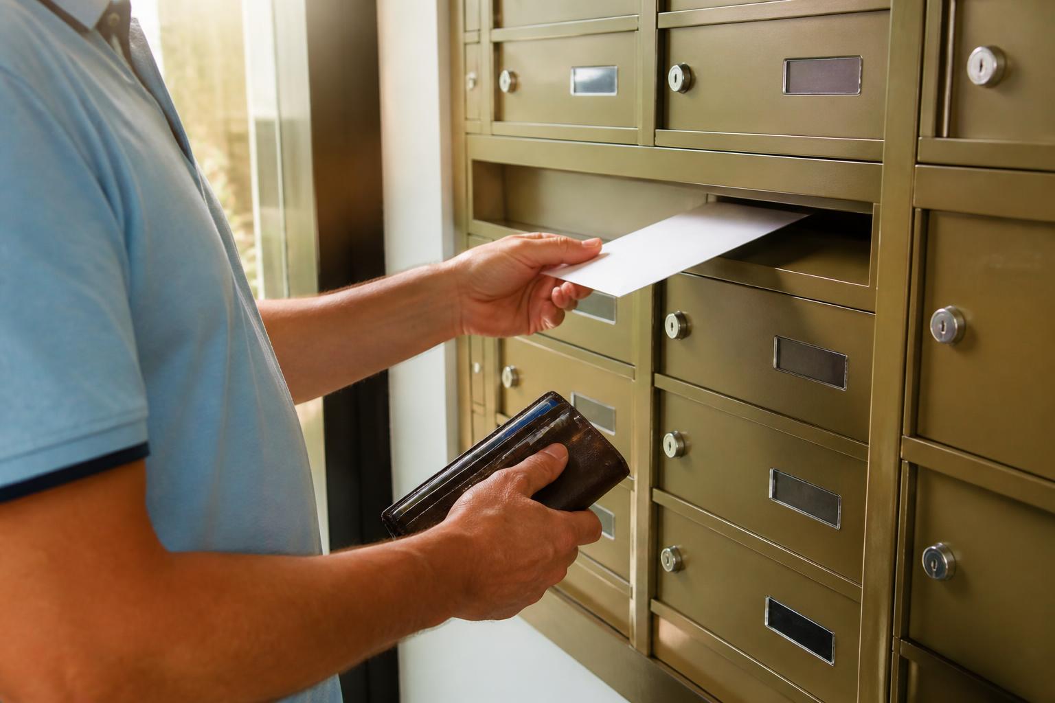 A person mailing a payoff envelope from an apartment mailroom.
