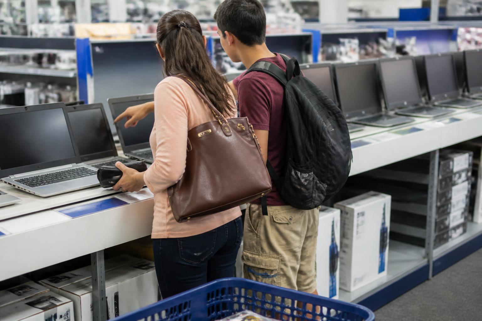 A parent and student comparing laptops in a generic electronics store.
