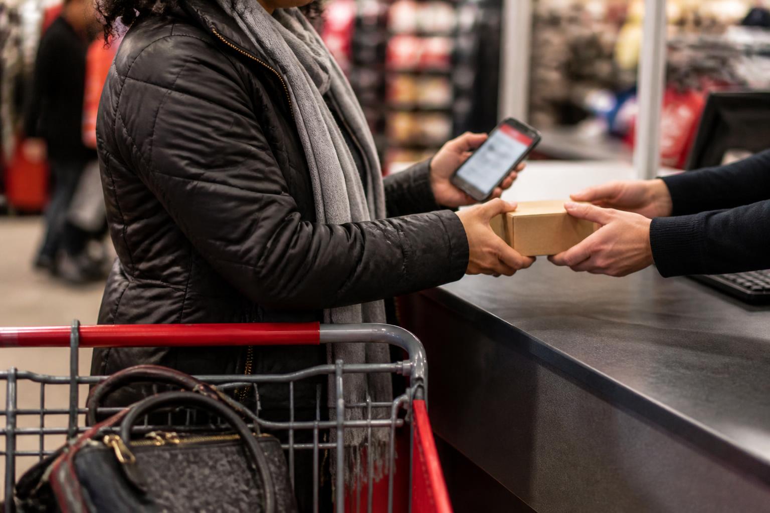 A shopper collecting one box at a customer service counter while checking a blurred fraud alert.