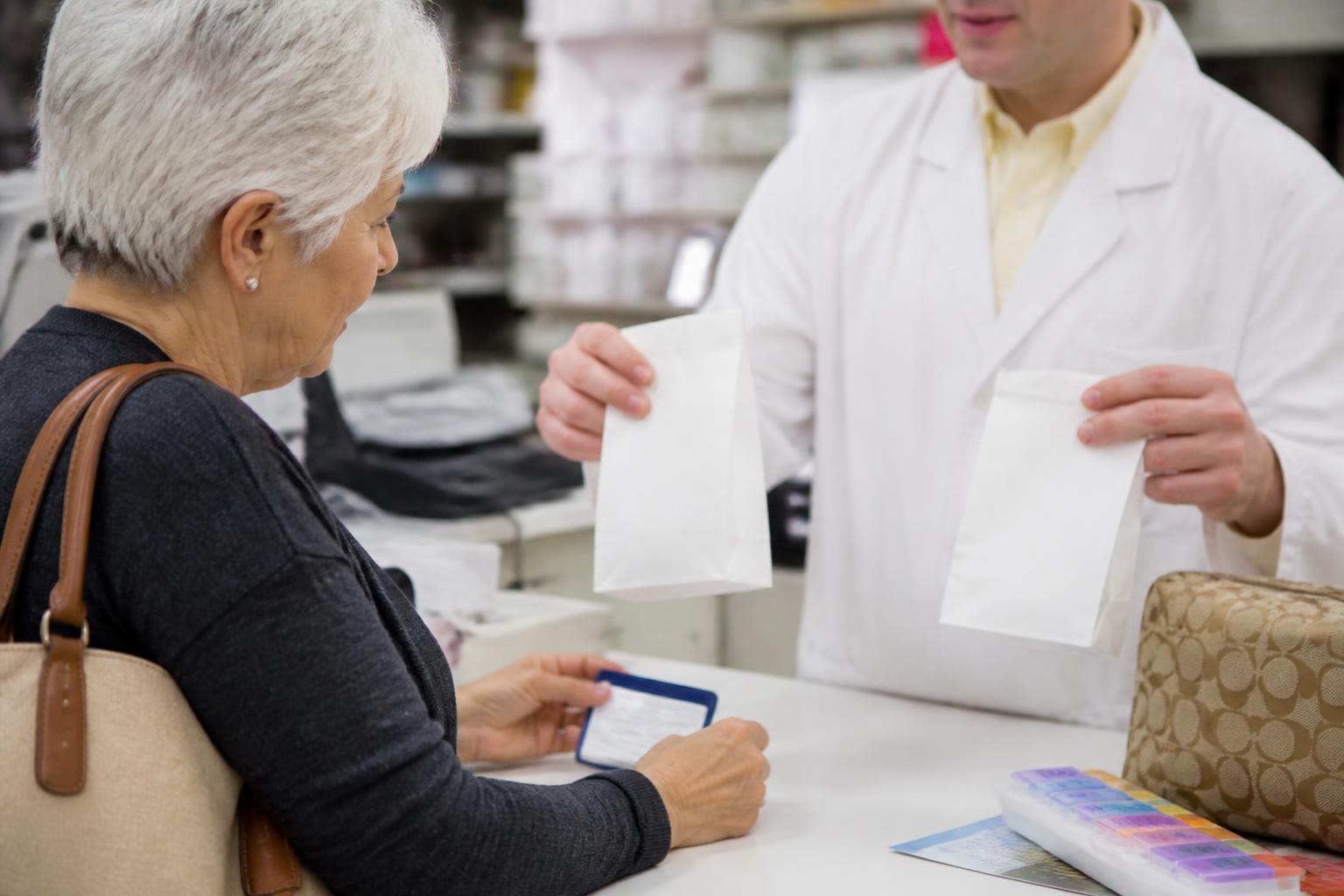 An older adult asking a pharmacist about prescription costs during open enrollment.
