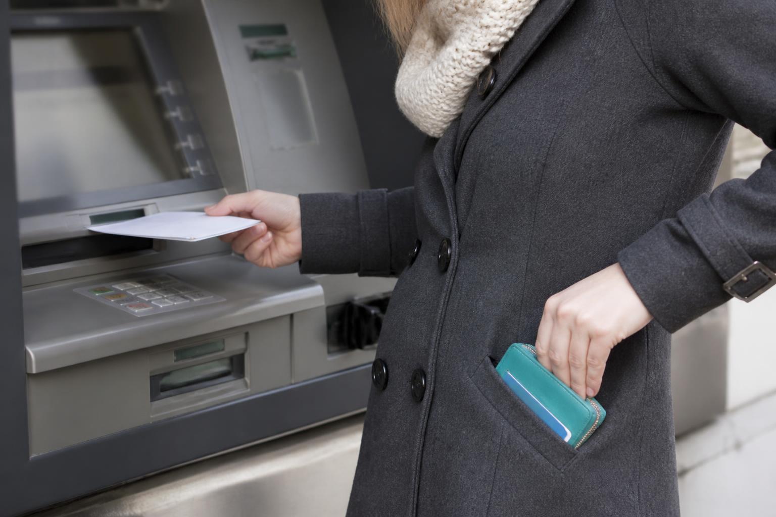 A taxpayer depositing a refund envelope at an ATM while saving part of it.