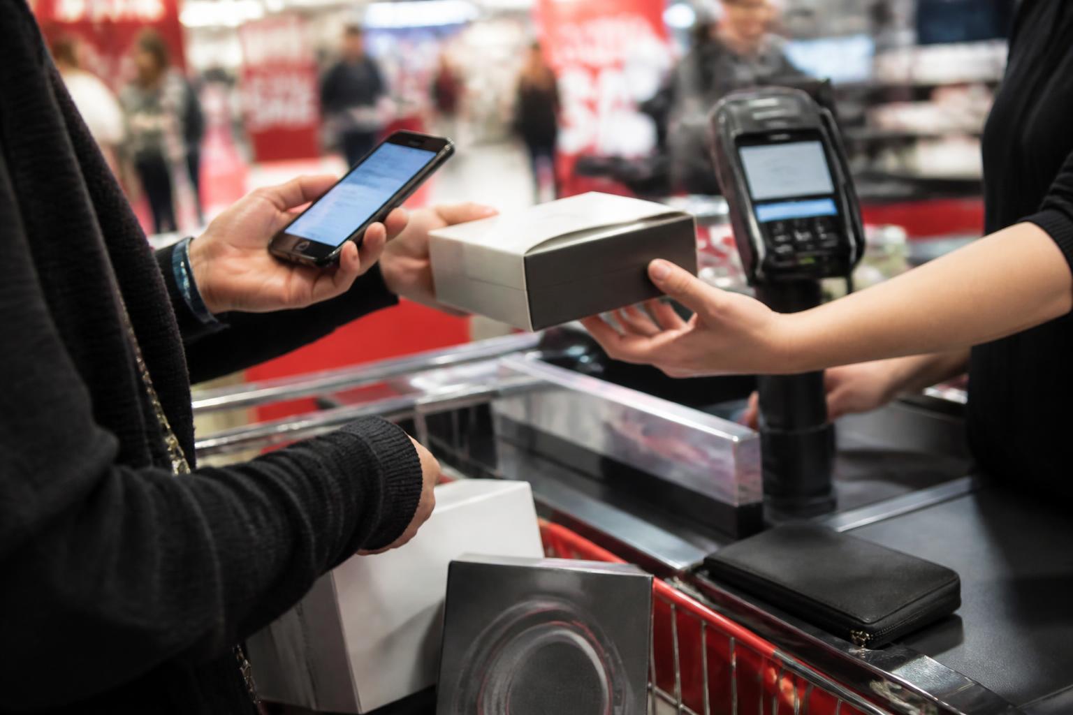 A shopper checking a blurred card alert at a retail checkout.