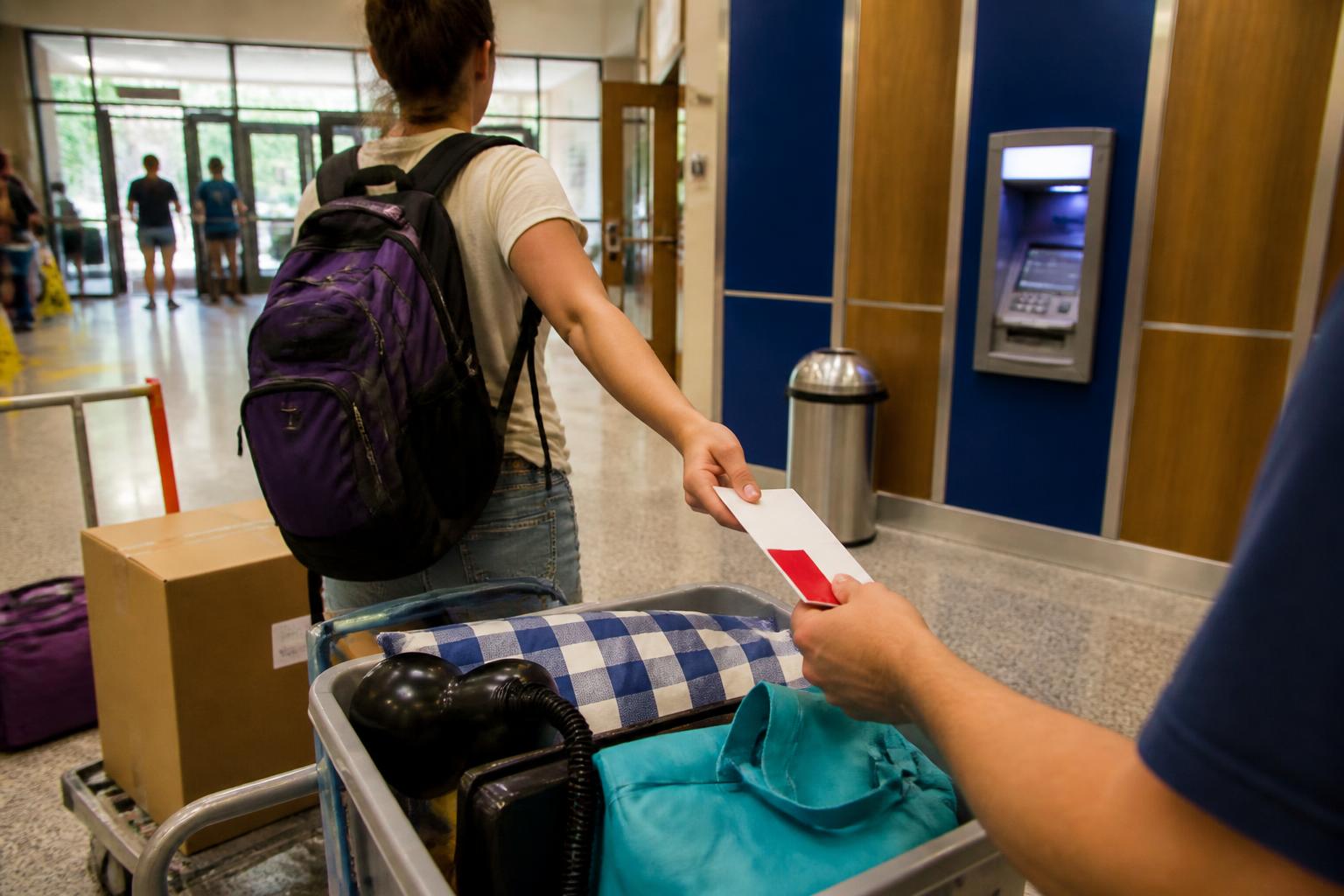 A parent handing a debit card sleeve to a student near a campus ATM.