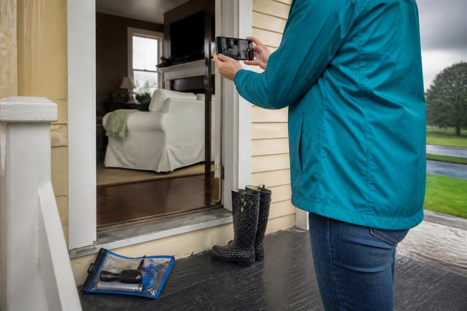 A homeowner photographing belongings from a covered porch before storm weather.