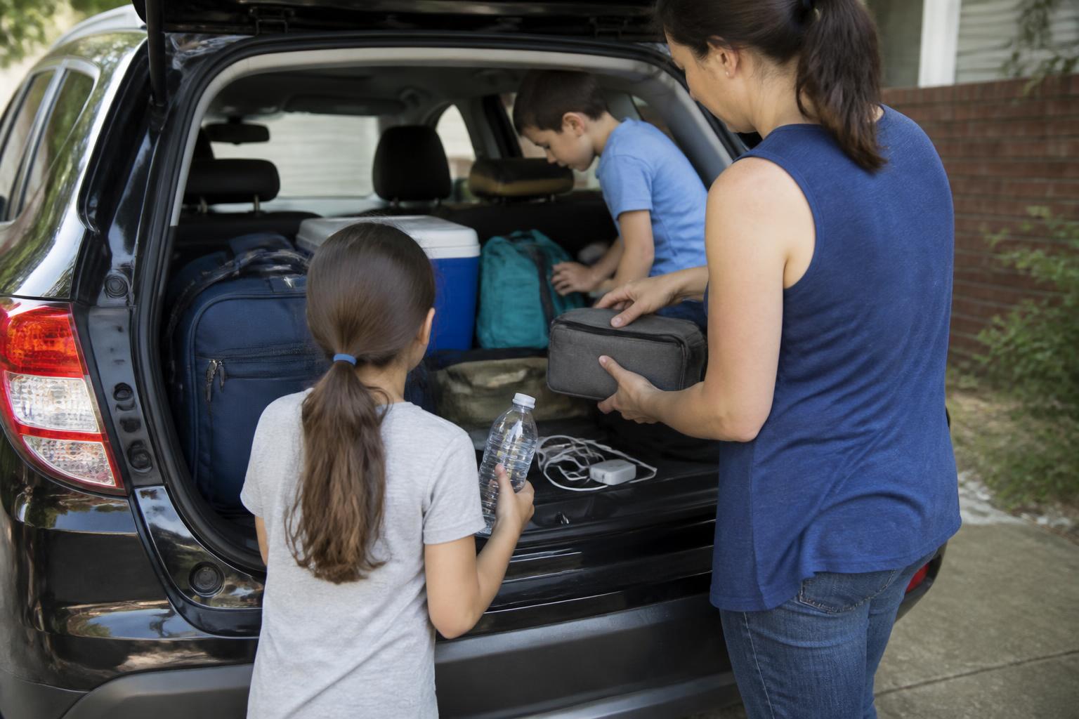 A family packing a car trunk with an emergency pouch before storm travel.