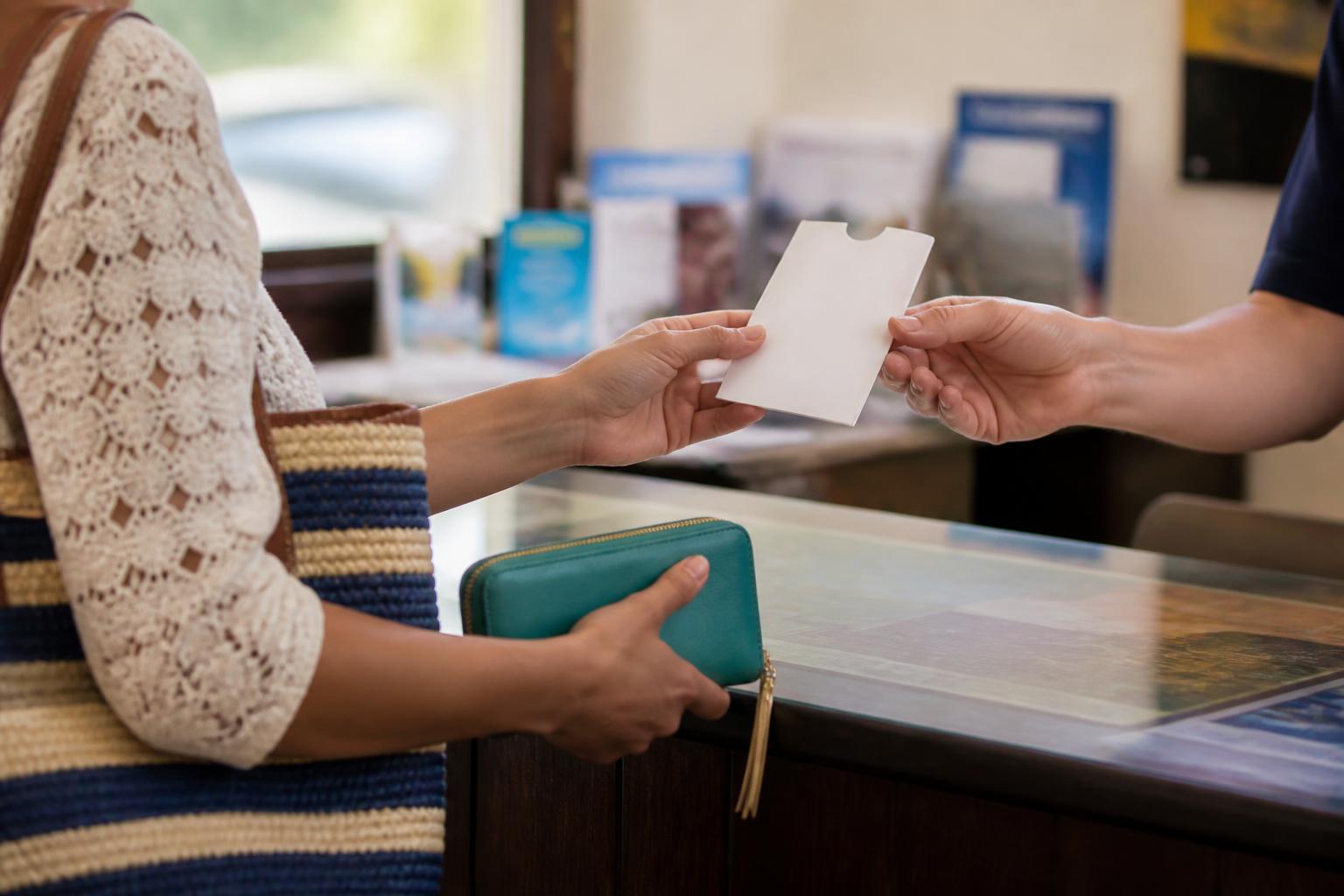 A traveler receiving a rental key while keeping a travel wallet zipped.
