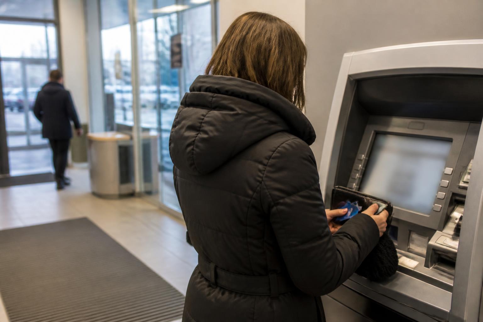A borrower checking an account balance at the ATM while moving a debit card back into a wallet.