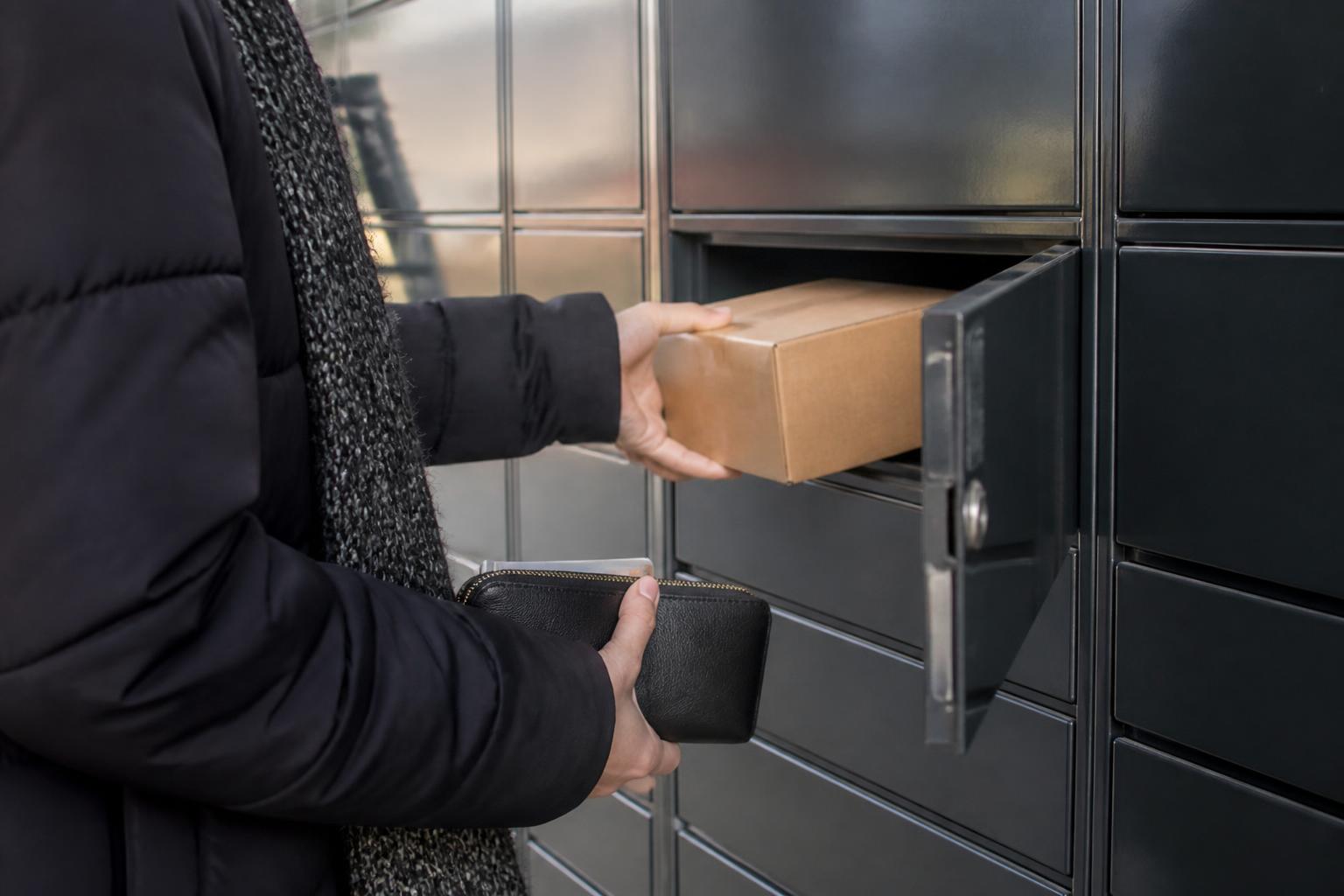 A holiday shopper placing one plain box into a locker while keeping a generic card inside a zipped wallet.