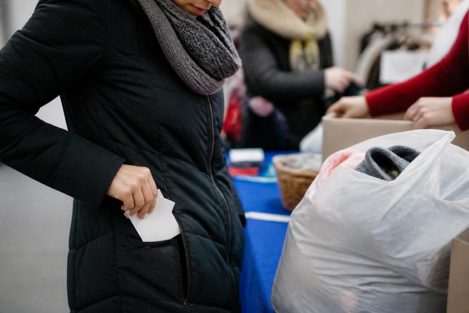 A donor placing a receipt into a coat pocket after setting down a bag of donated goods.