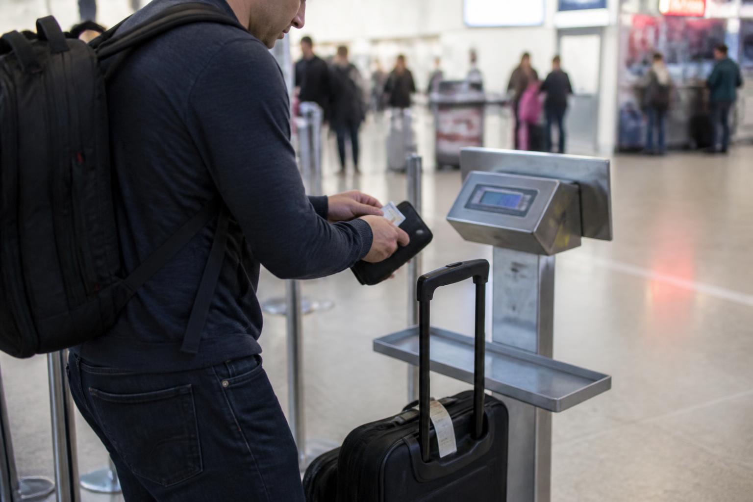 A traveler weighing a carry-on while putting away a travel card.