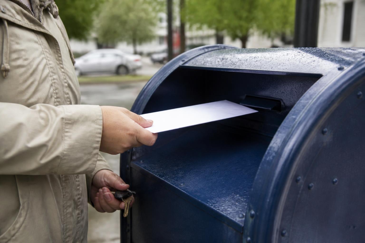 A taxpayer sliding a sealed payment envelope into the collection slot while holding keys in the other hand.