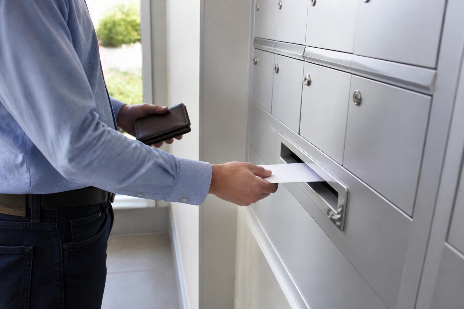 A cardholder placing a sealed payment envelope into outgoing mail while holding a closed wallet.