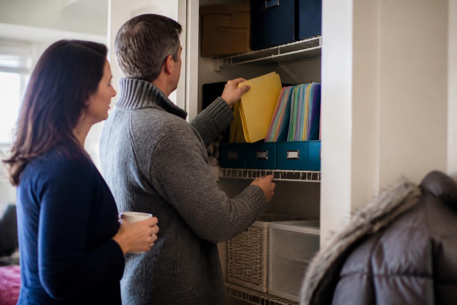 A policyholder pulling an insurance folder from a color-coded file bin while standing in the closet doorway.