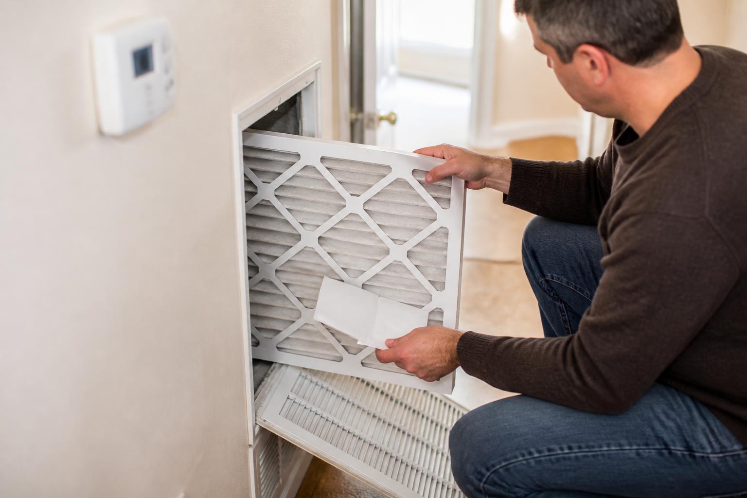A homeowner replacing an air filter during a utility-savings check.