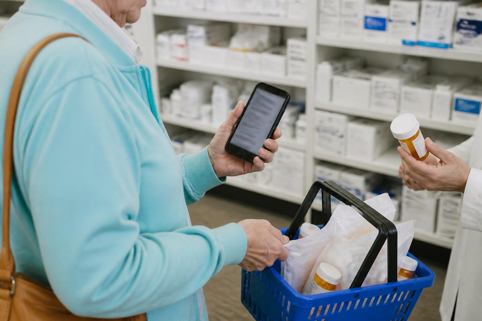 An older adult checking a medication list on a blurred phone while comparing generic prescription bags in a basket.
