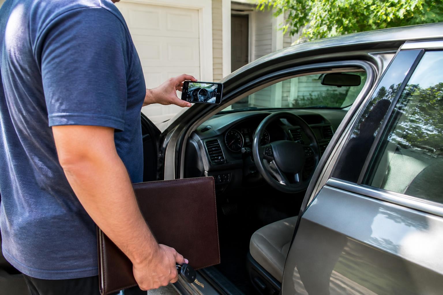 A driver photographing car mileage before calling an auto insurer.