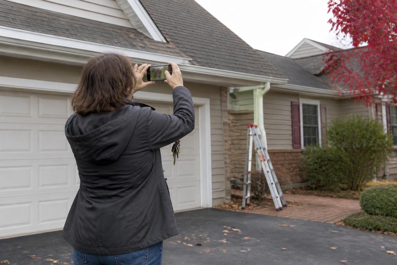 A homeowner photographing the exterior of the house while reviewing deductible exposure.