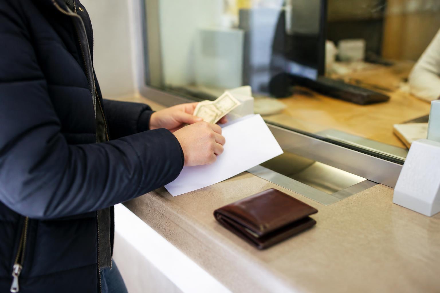 A customer setting aside January bill money at a bank teller window.