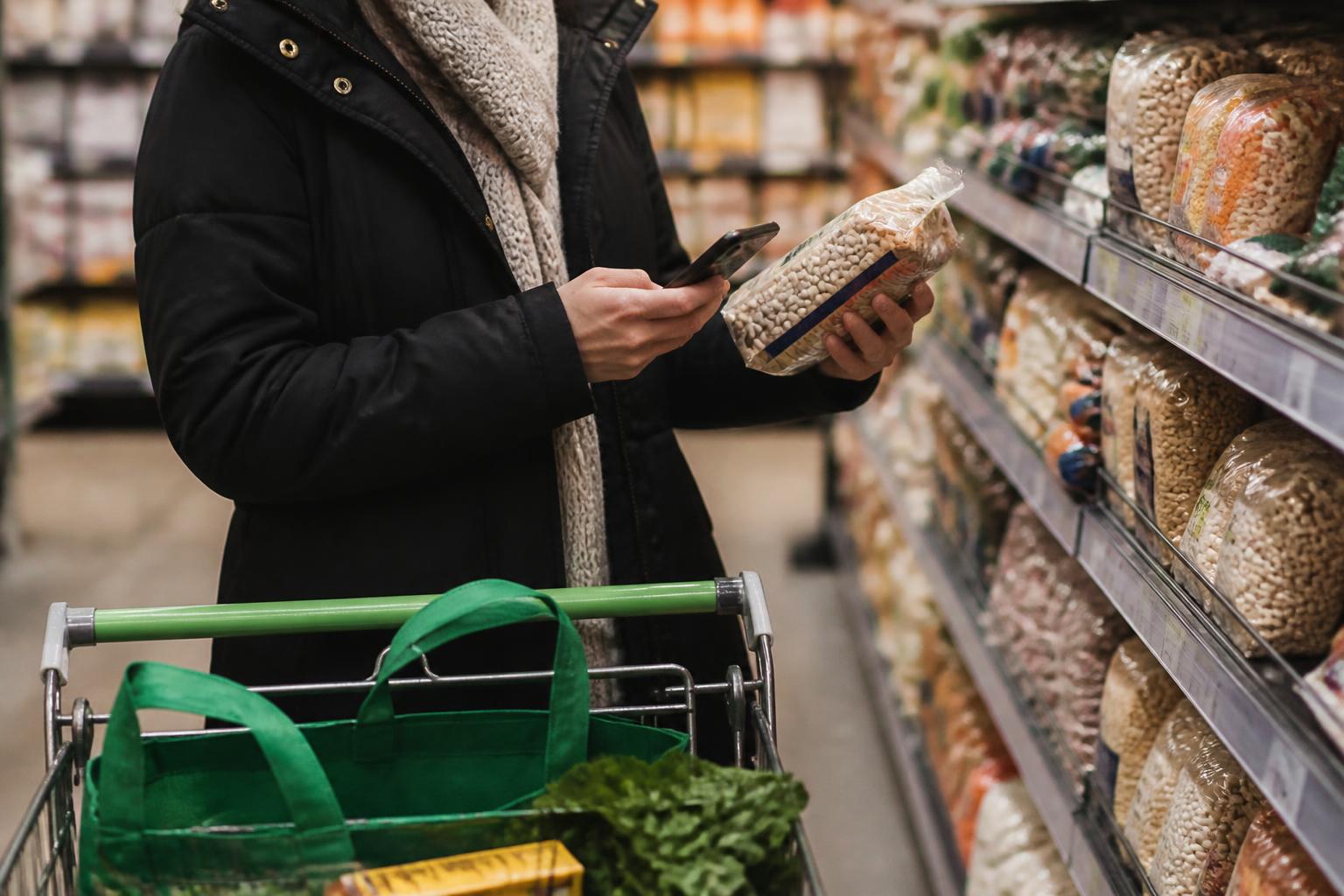 A shopper comparing pantry staples while checking a reminder.