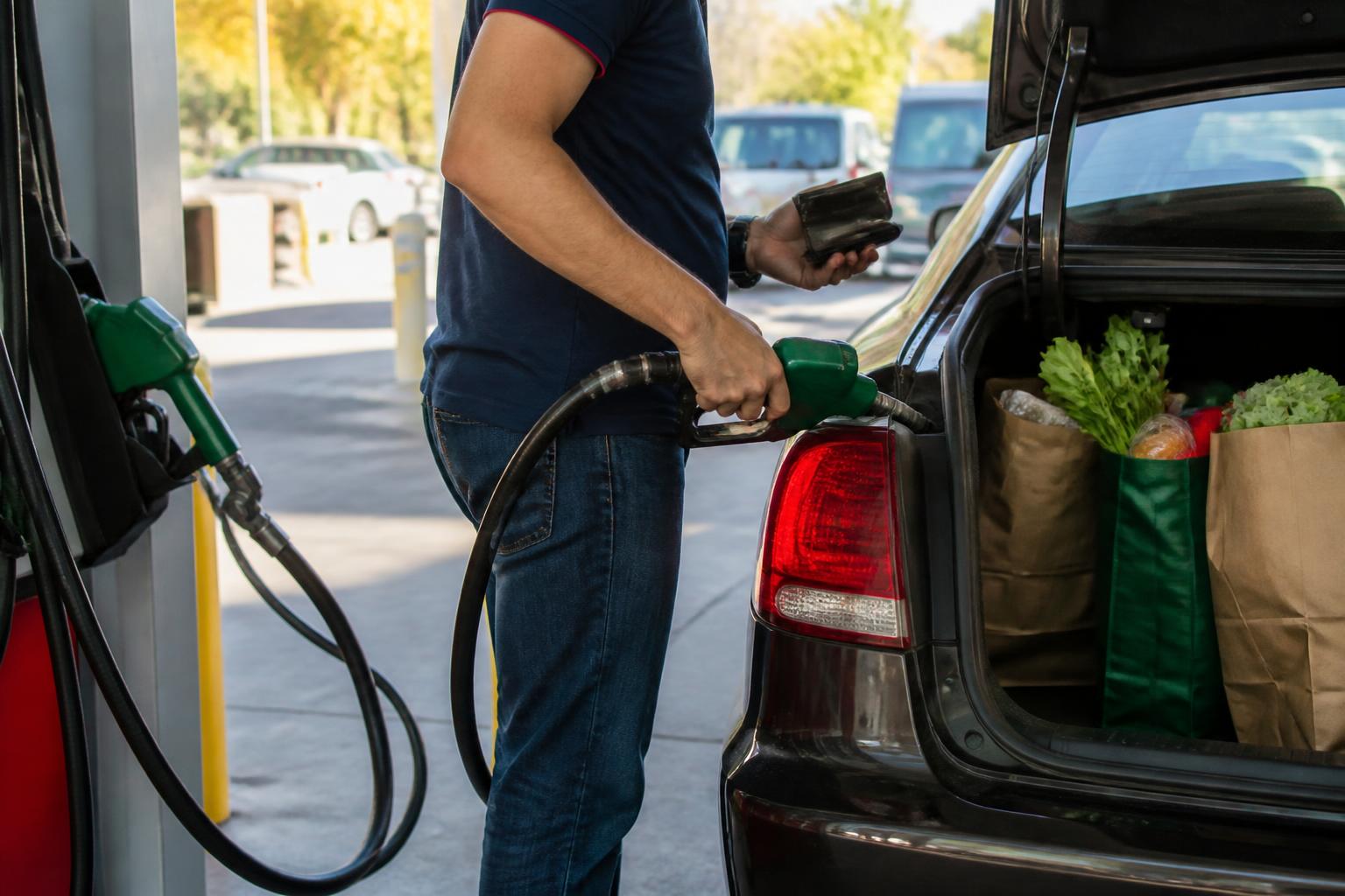 A driver loading groceries at a gas station during a grocery-and-gas reset.