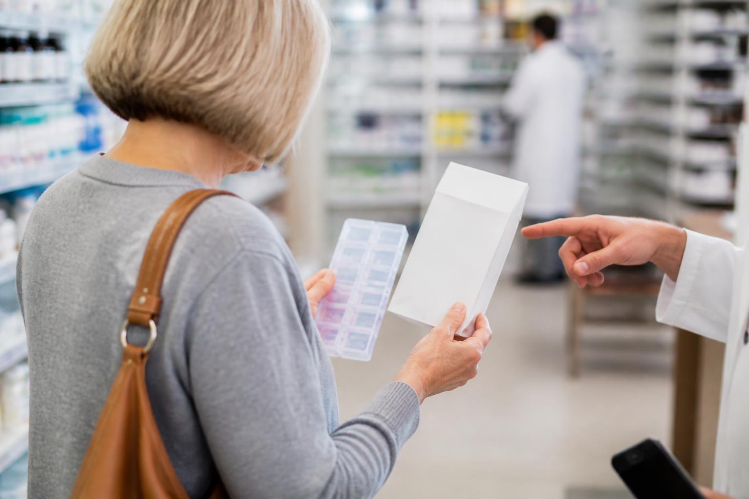 An older adult comparing a pill organizer in a pharmacy aisle.