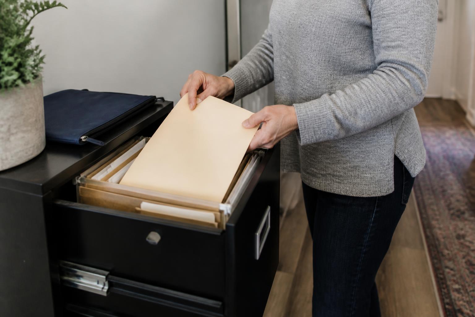 A person filing sealed tax records in a home file drawer.