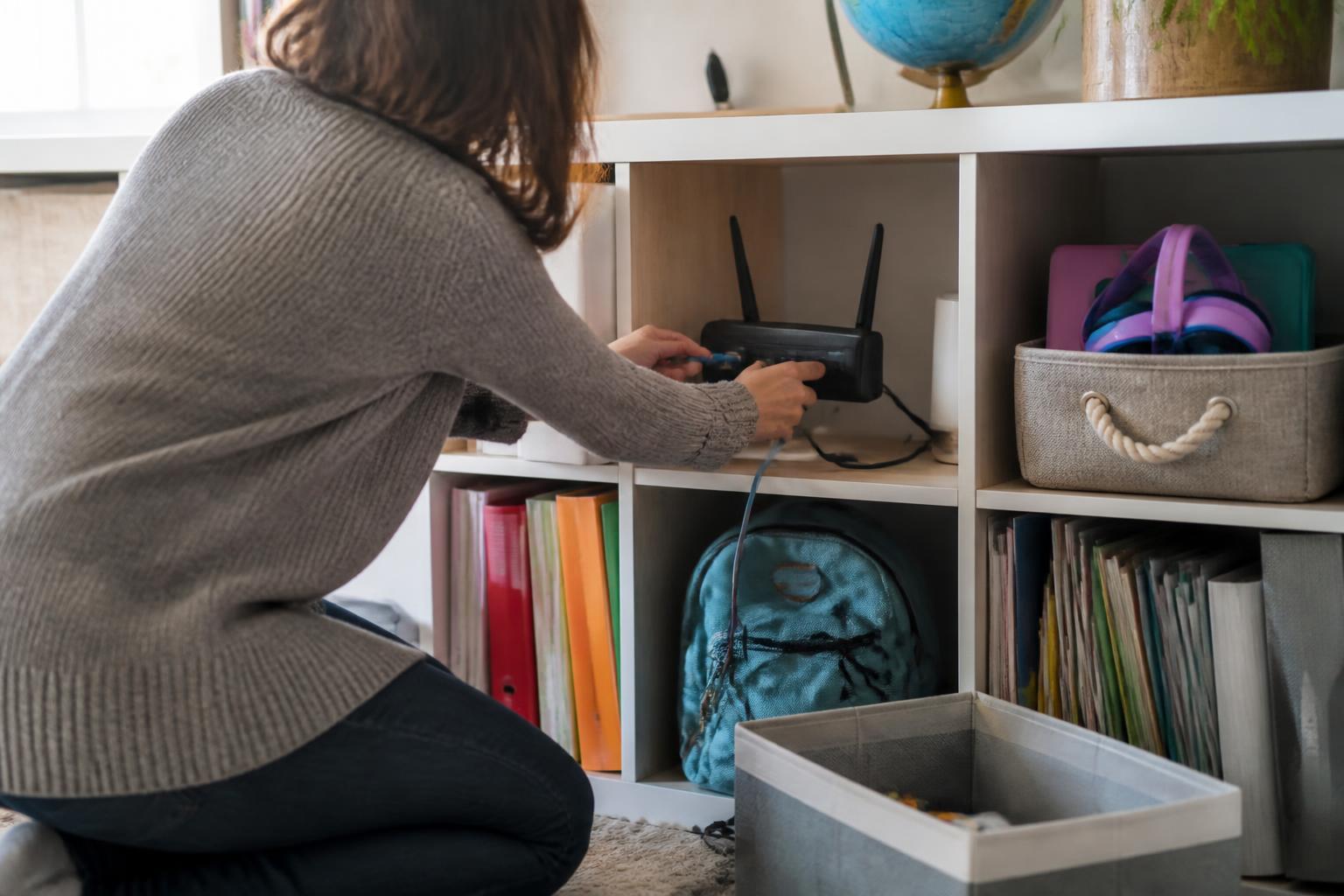 A parent connecting remote-school equipment on a family learning shelf.