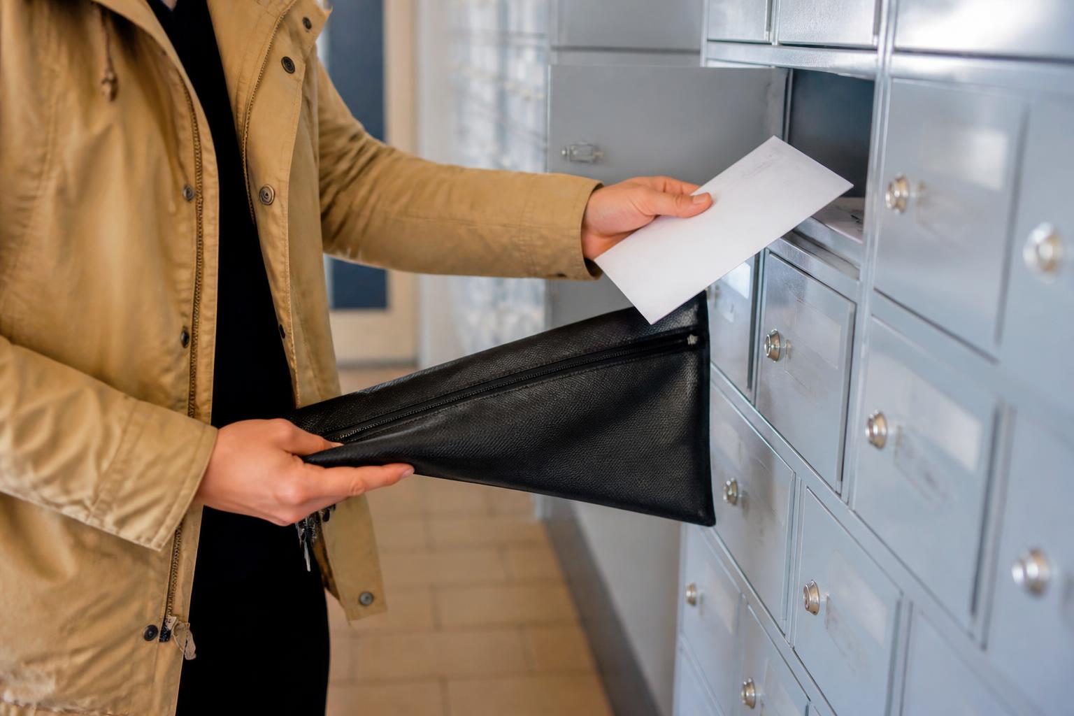 A renter securing mail in a document pouch in an apartment mailroom.