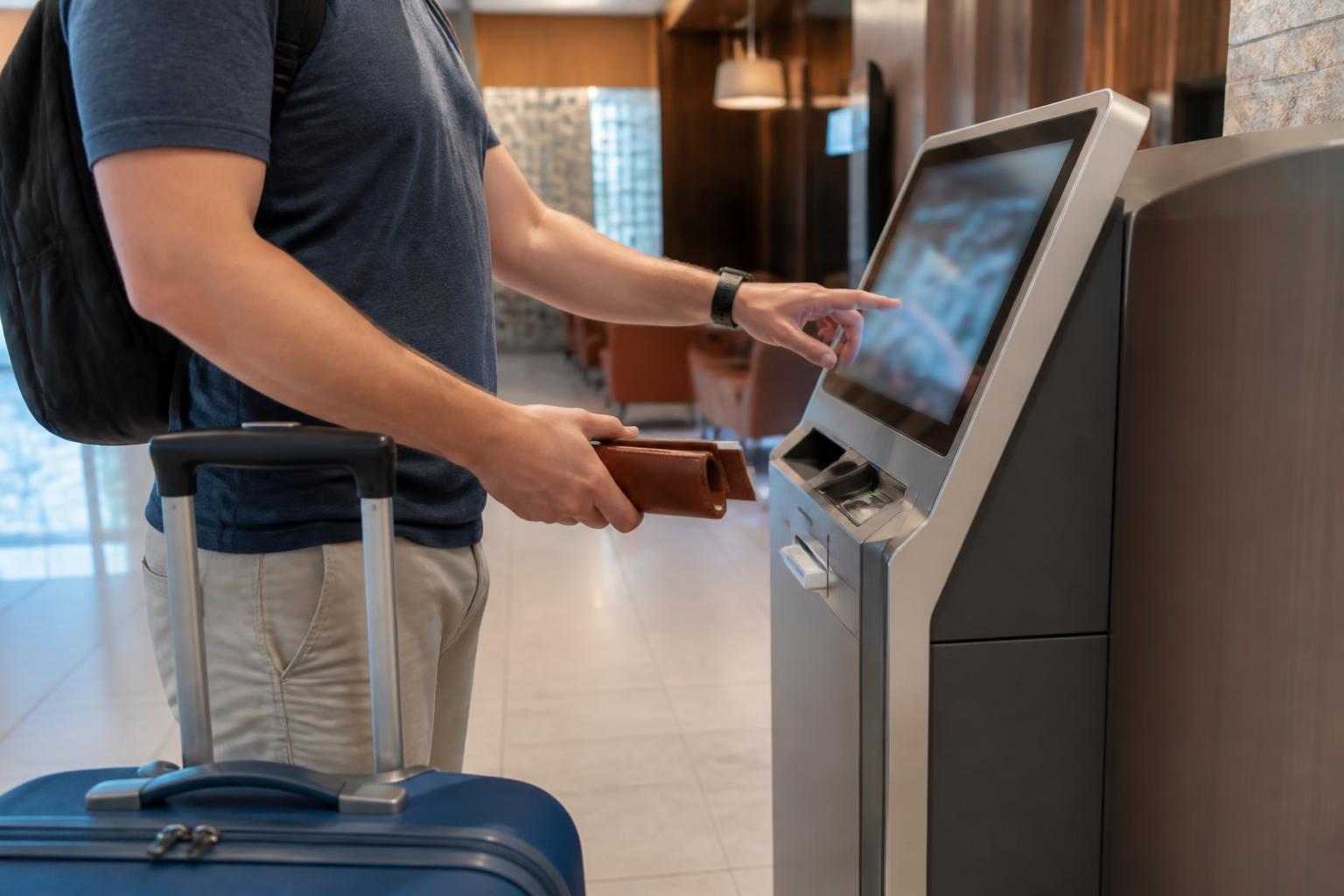 A traveler using a hotel self-check-in kiosk with luggage nearby.