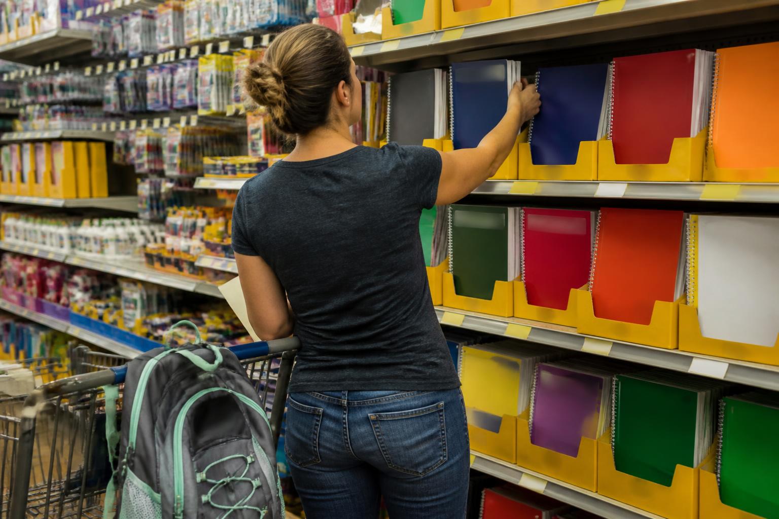 A shopper selecting school supplies from a store aisle.