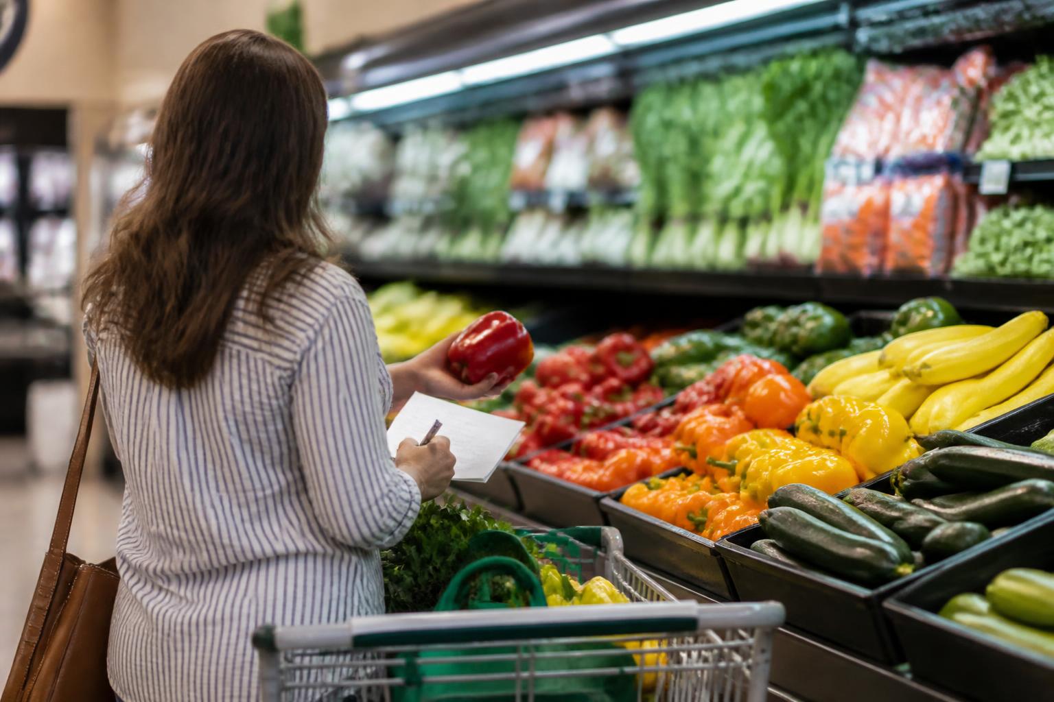 A shopper comparing produce in a supermarket aisle.