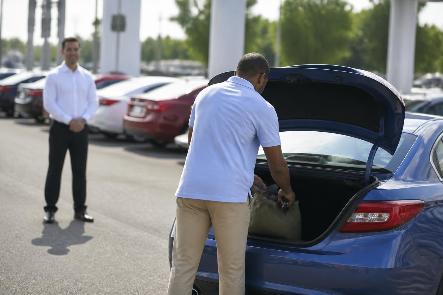 A driver emptying a trade-in trunk at a service lane.
