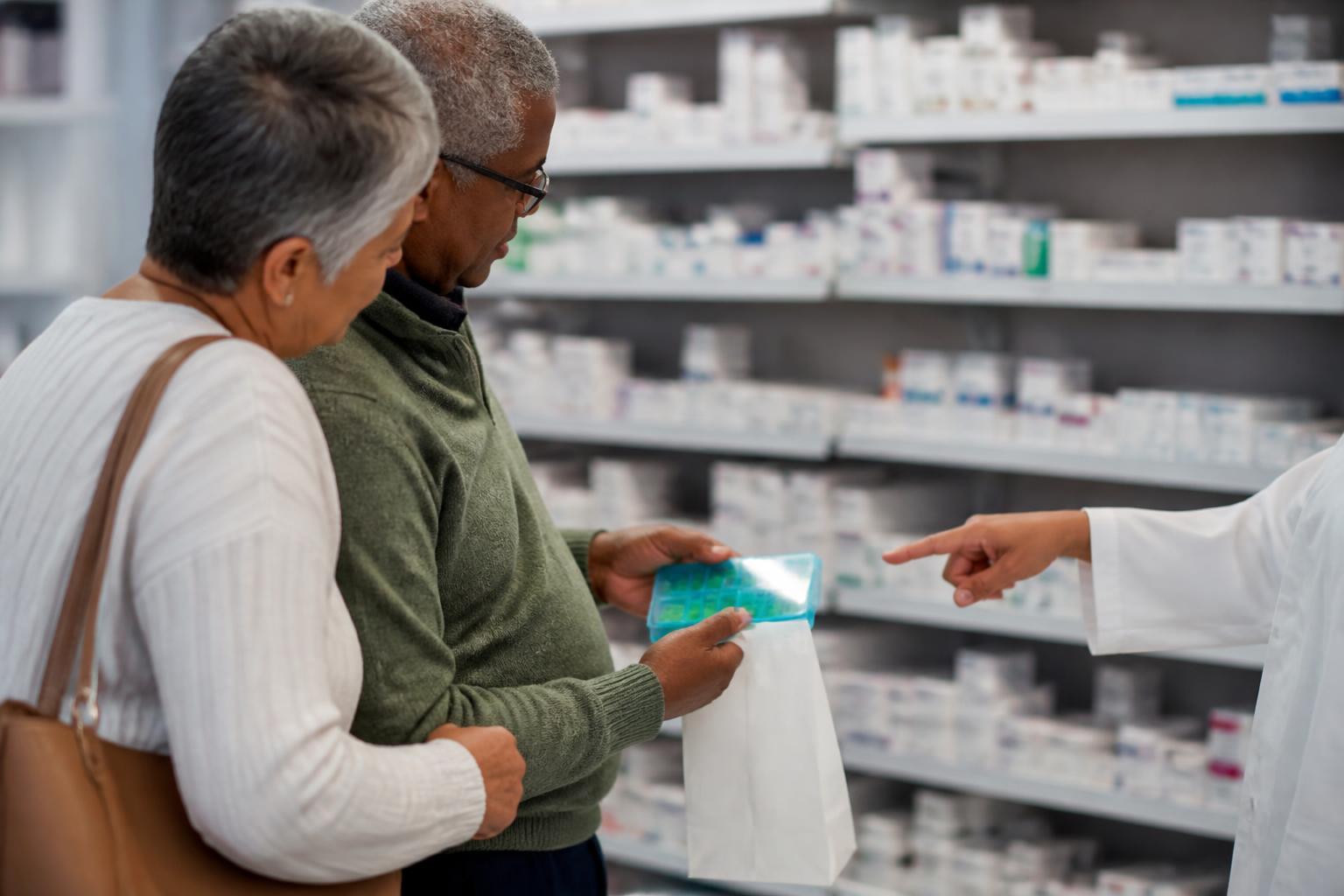 An older adult comparing a pill organizer in a pharmacy aisle.
