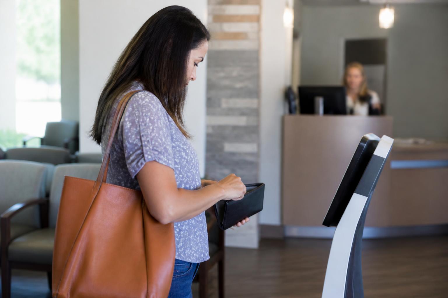 A patient checking a wallet near a clinic payment kiosk.