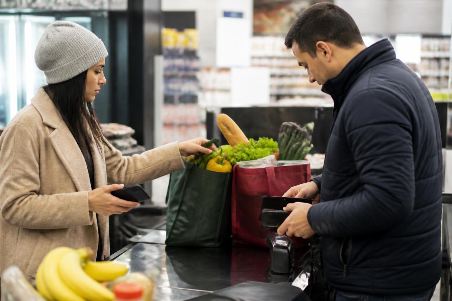 Two partners dividing groceries at checkout while handling shared bills.