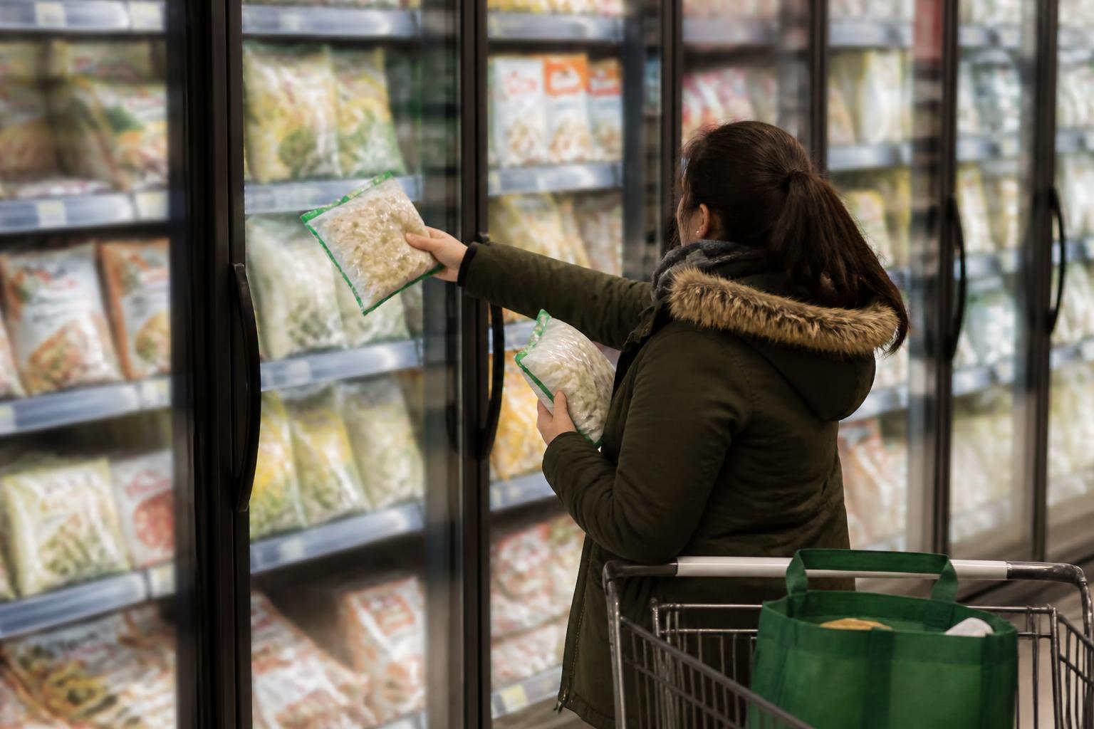 A shopper comparing frozen groceries while budgeting for 2024.