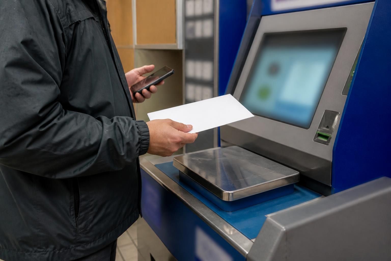 A taxpayer weighing a sealed envelope at a post office kiosk.