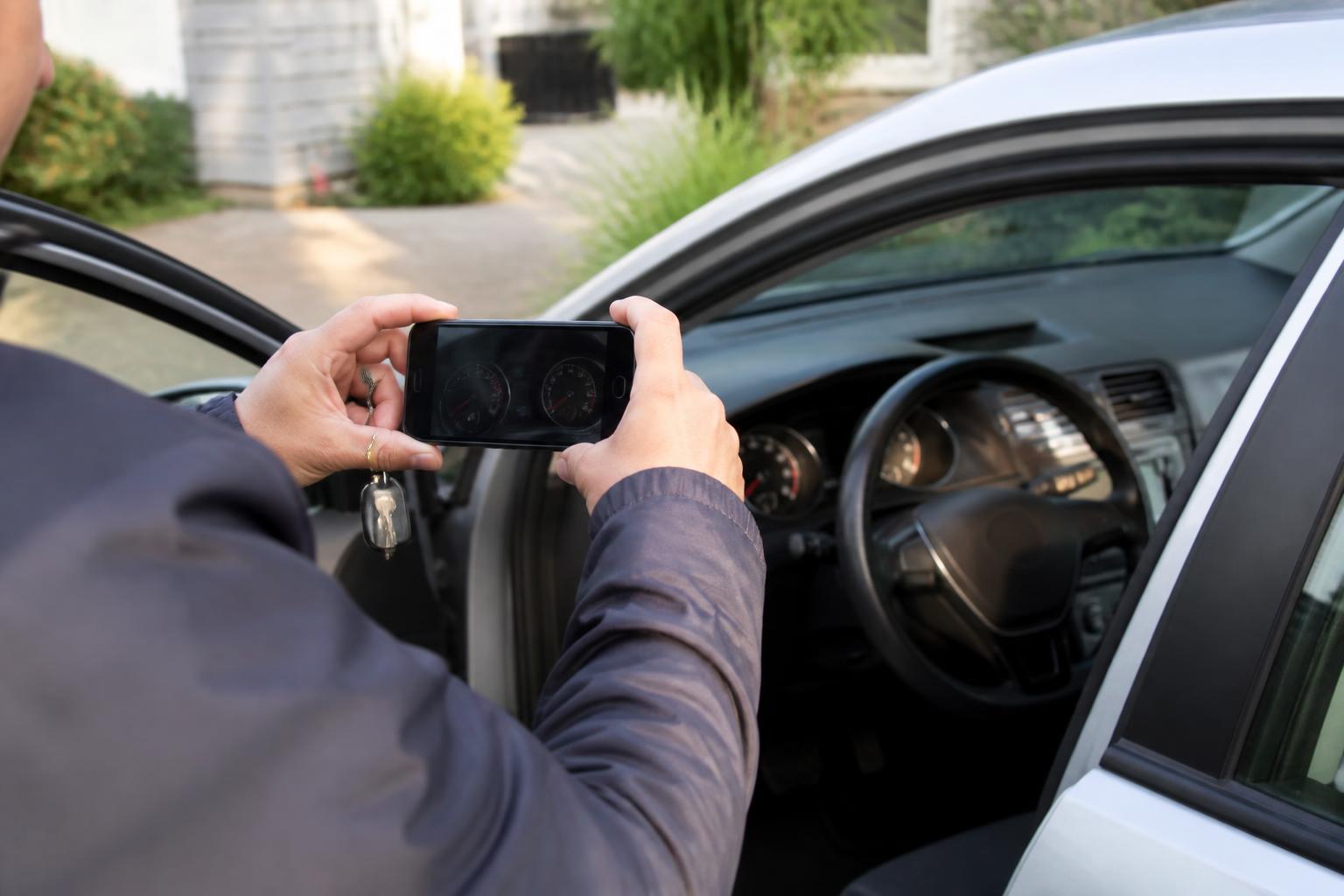 A driver photographing mileage through an open car door.