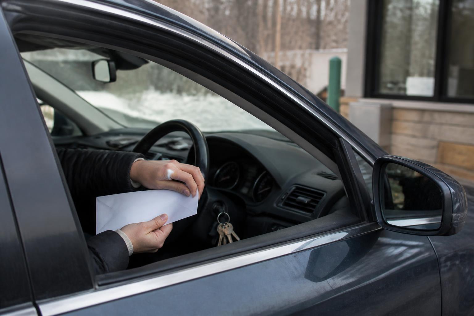 A borrower preparing a plain payment envelope in a credit-union drive-up lane.
