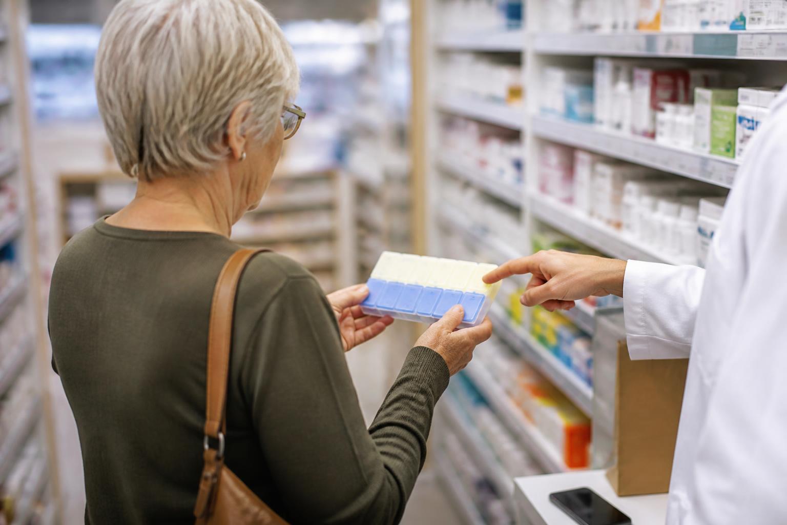 An older adult comparing a pill organizer in a pharmacy aisle.