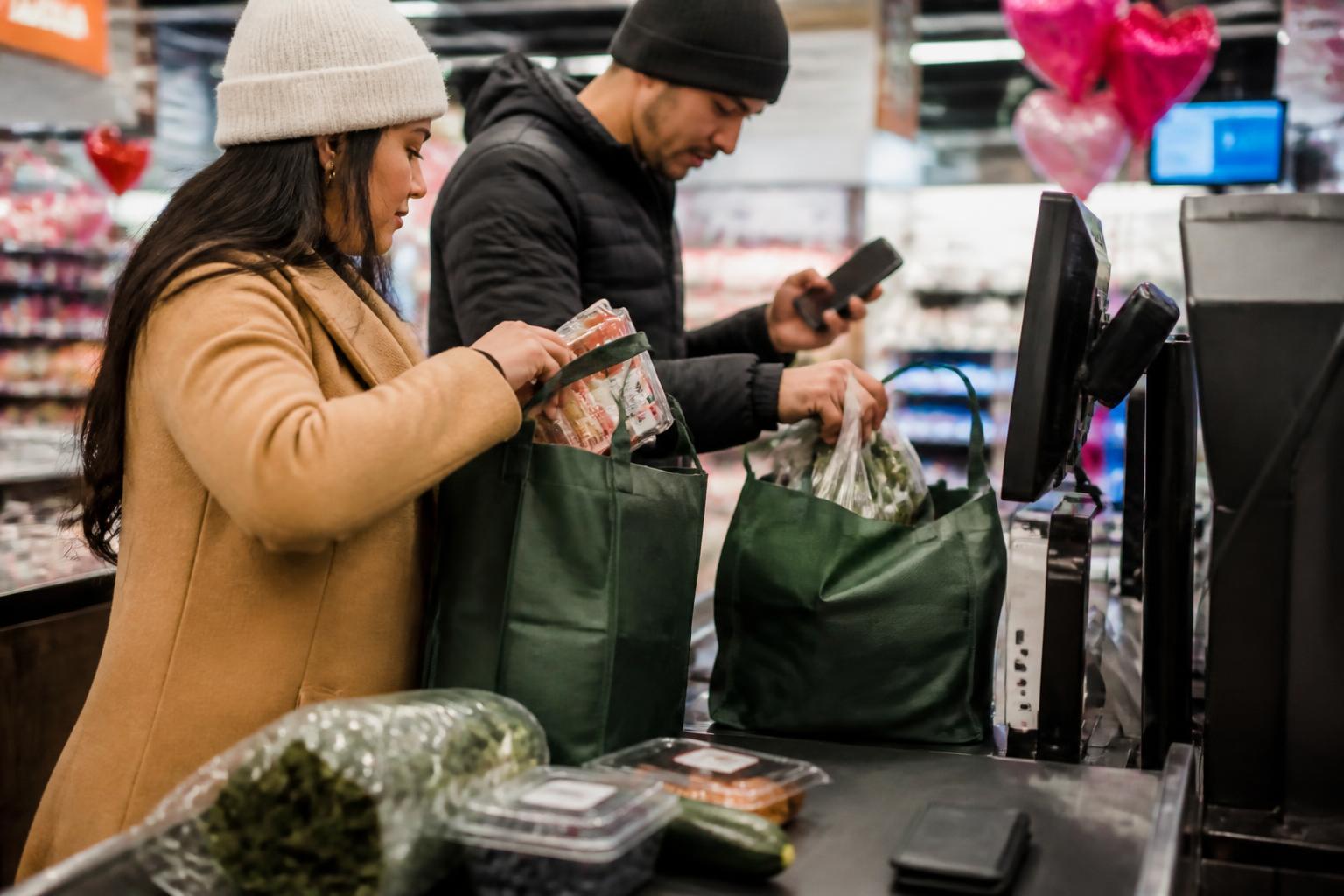 Two adults dividing groceries while checking a shared-spending alert.